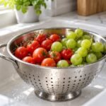 How to clean a colander: stainless steel colander of rinsed tomatoes and grapes in a sink